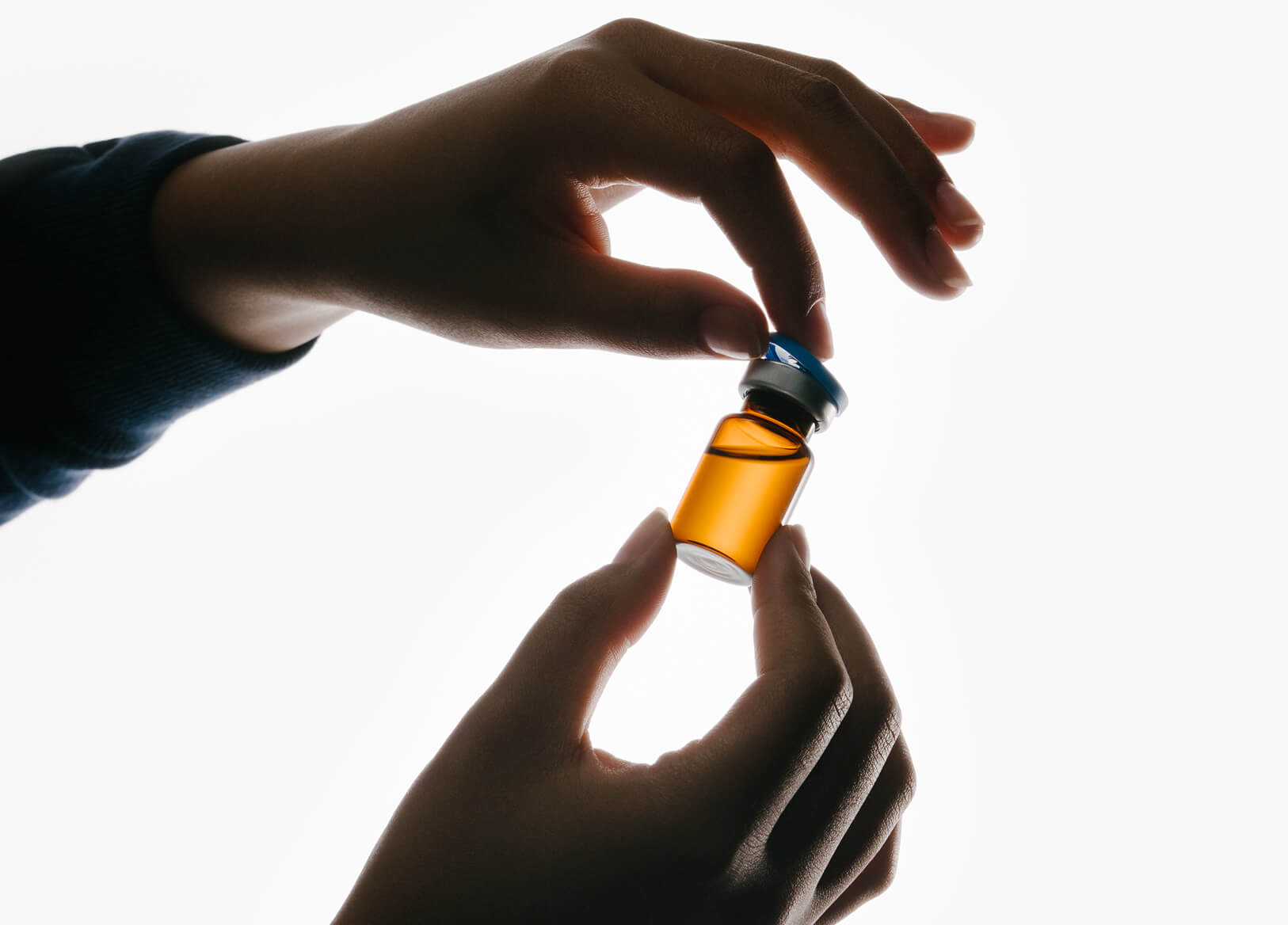 Hands opening an amber vial of compounded medication